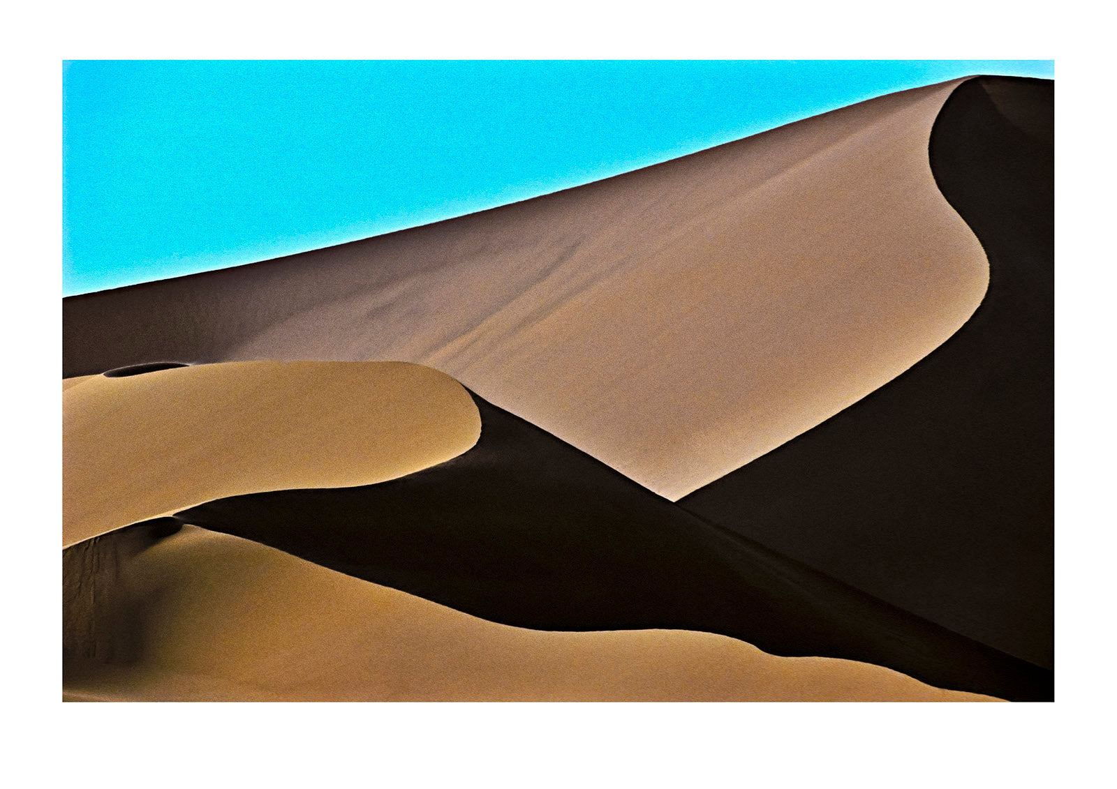 The elegant crest of a vast sand dune in shadow against a blue sky. near Sossusvlei, Great Southern Dune Field, Namib-Naukluft National Park, Namibia.