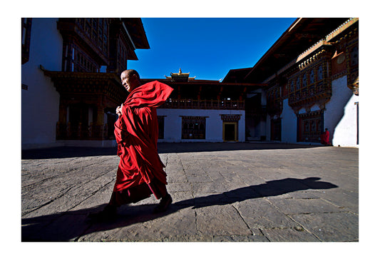 A brisk wind catches the flaming-red robes of a Buddhist monk as he strides purposefully between prayers in a Himalayan valley in Bhutan.