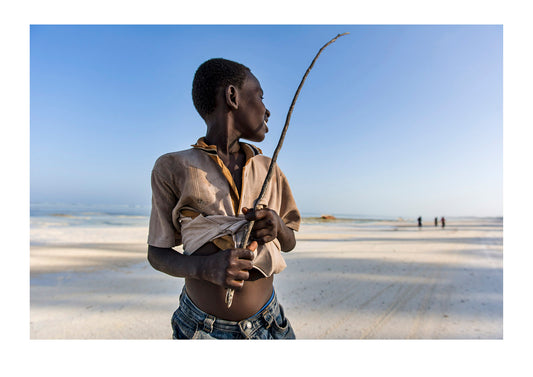 A young boy herding his family cattle along a deserted beach is distracted by the calls from his young siblings and the reprimands of his father. Zanzibar.