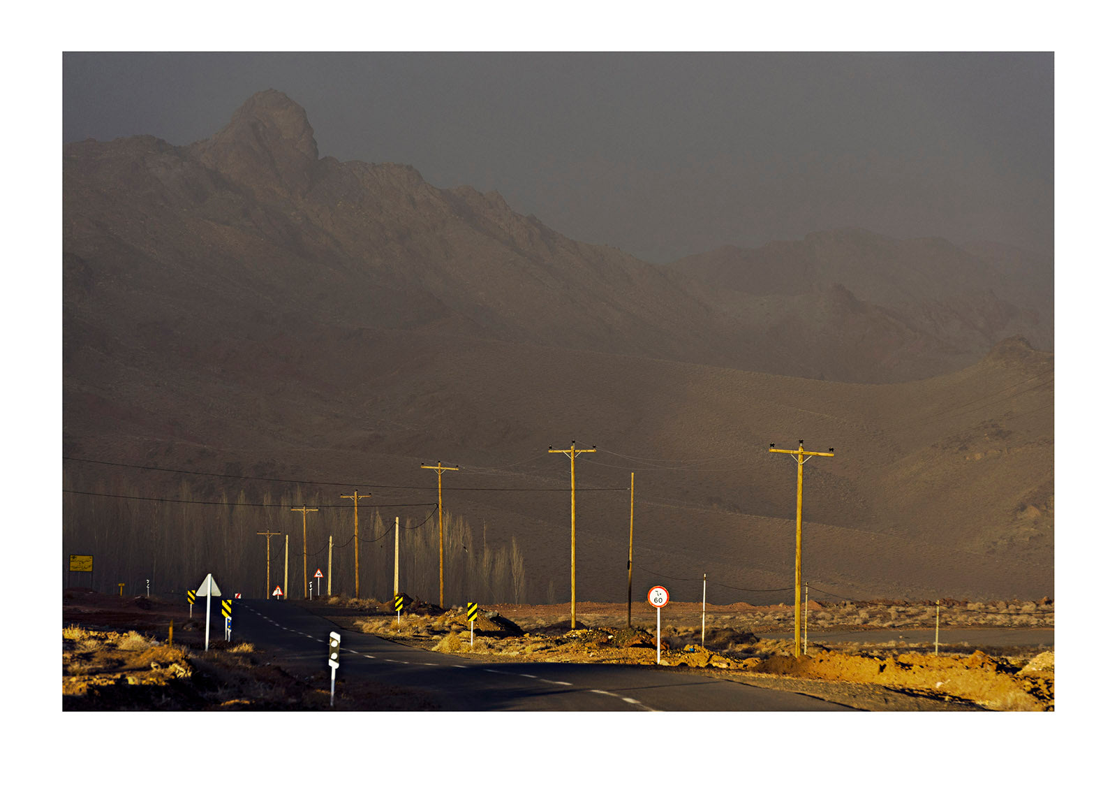 A sunray pierces a storm and lights electricity poles running through a mountain pass. Abyaneh village, Abyaneh, Barzrud Rural District, Natanz County, Isfahan Province, Islamic Republic of Iran.

