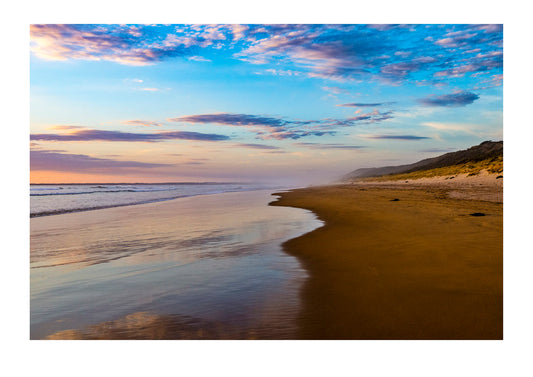 As the tide recedes along a wide beach the sunset afterglow is reflected in the wet sand. Venus Bay, Victoria, Australia.