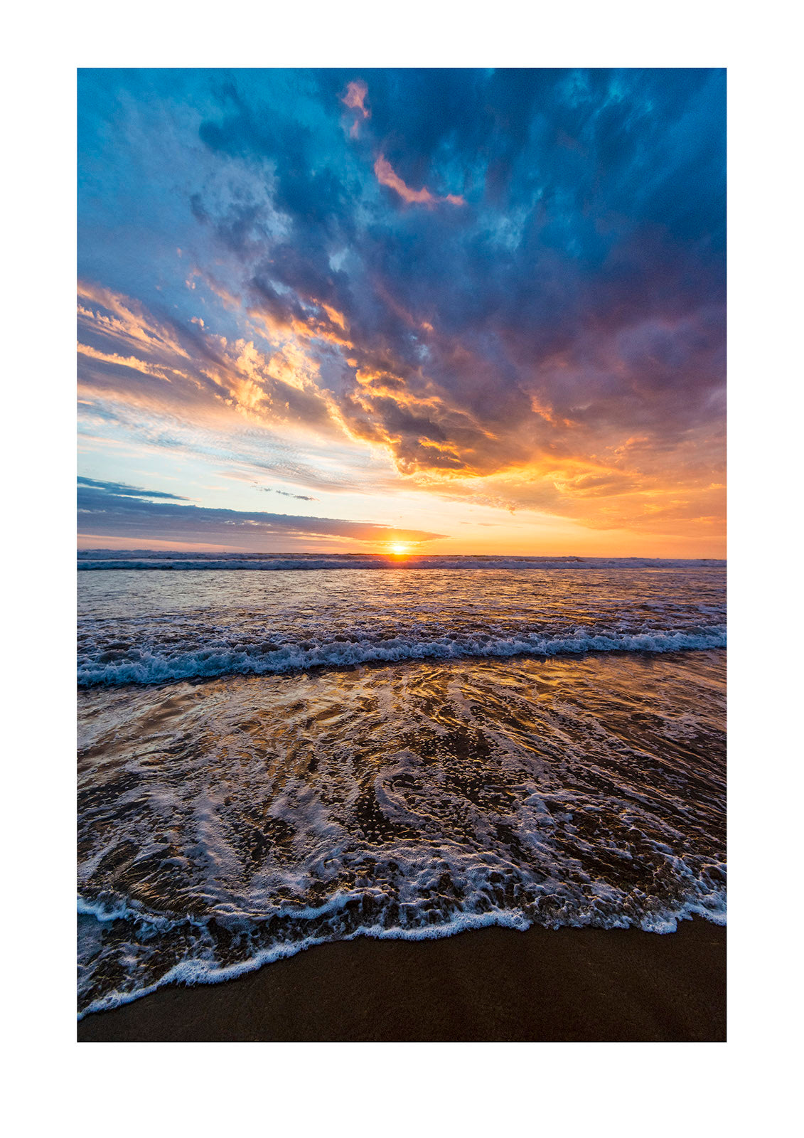 Beneath a storm front an incoming tide pushes waves onto a beach at sunset. Venus Bay, Victoria, Australia.