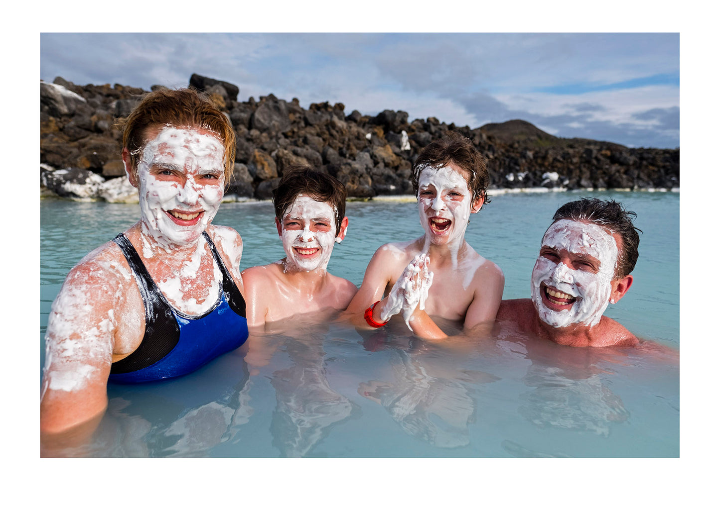 Having lathered their faces in mineral mud, a family bathes in the geothermal hot springs at the Blue Lagoon. Blue Lagoon, Iceland.