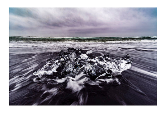 A raging sea casts waves onto a black volcanic sand beach and glacier iceberg. Iceland. 