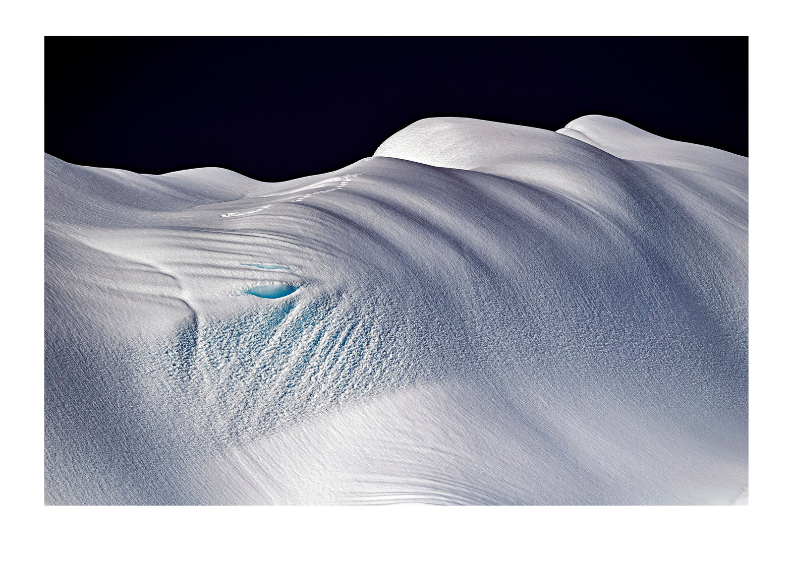 Sunlight reflecting off the silky, satin snow-covered surface of a large iceberg before a descending storm. Antarctic Peninsula, Antarctica.