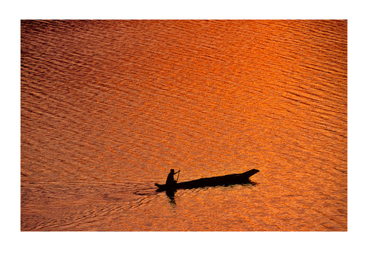 A fisherman in a dugout canoe on a golden lake surface at dawn. Lake Mutanda, Kisoro District, South Western Uganda.